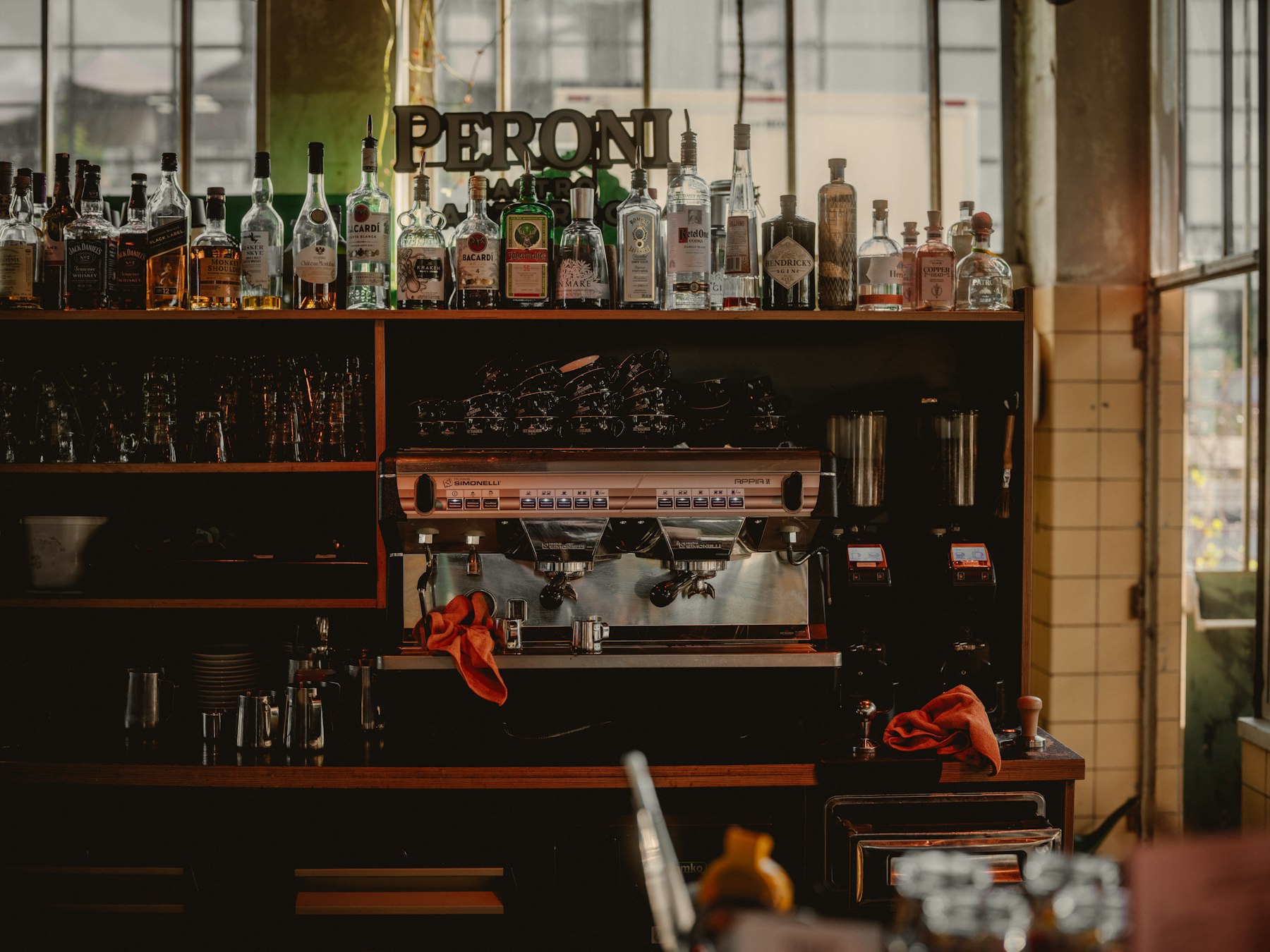 Restaurant bar counter with an espresso machine, shelves of spirits and glasses, and a brand sign above